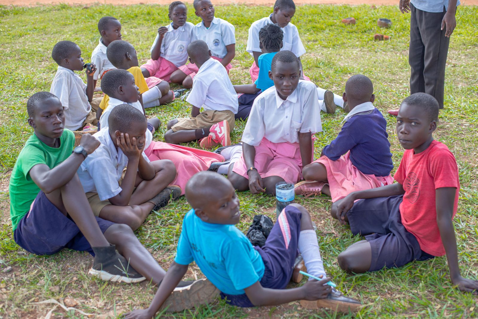 Pupils at Gulu Primary School sitting in a circle on the grass during an ASAT practical